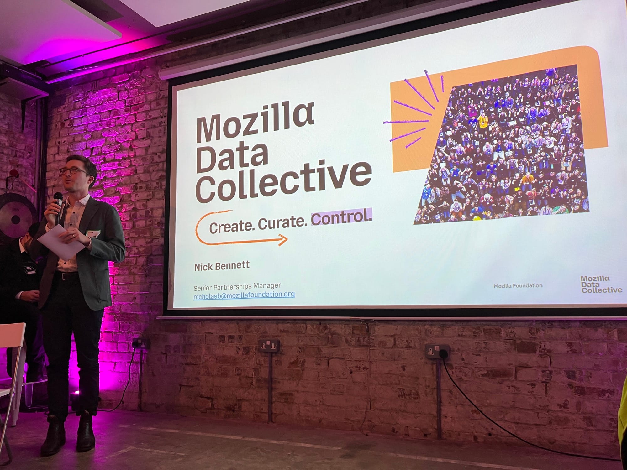 Nick Bennet speaks in front of a slide: Mozilla Data Collective → Create. Curate. Control.