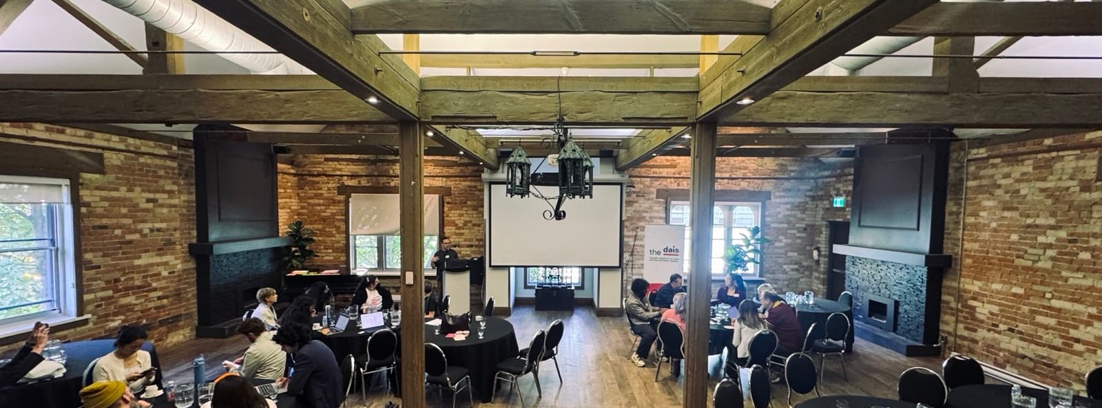 Chad speaks at a podium in a large brick room with wooden beams