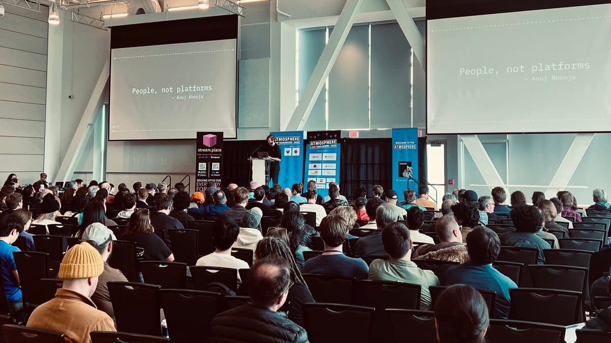 Paul stands on a stage with two large projection screens addressing an audience