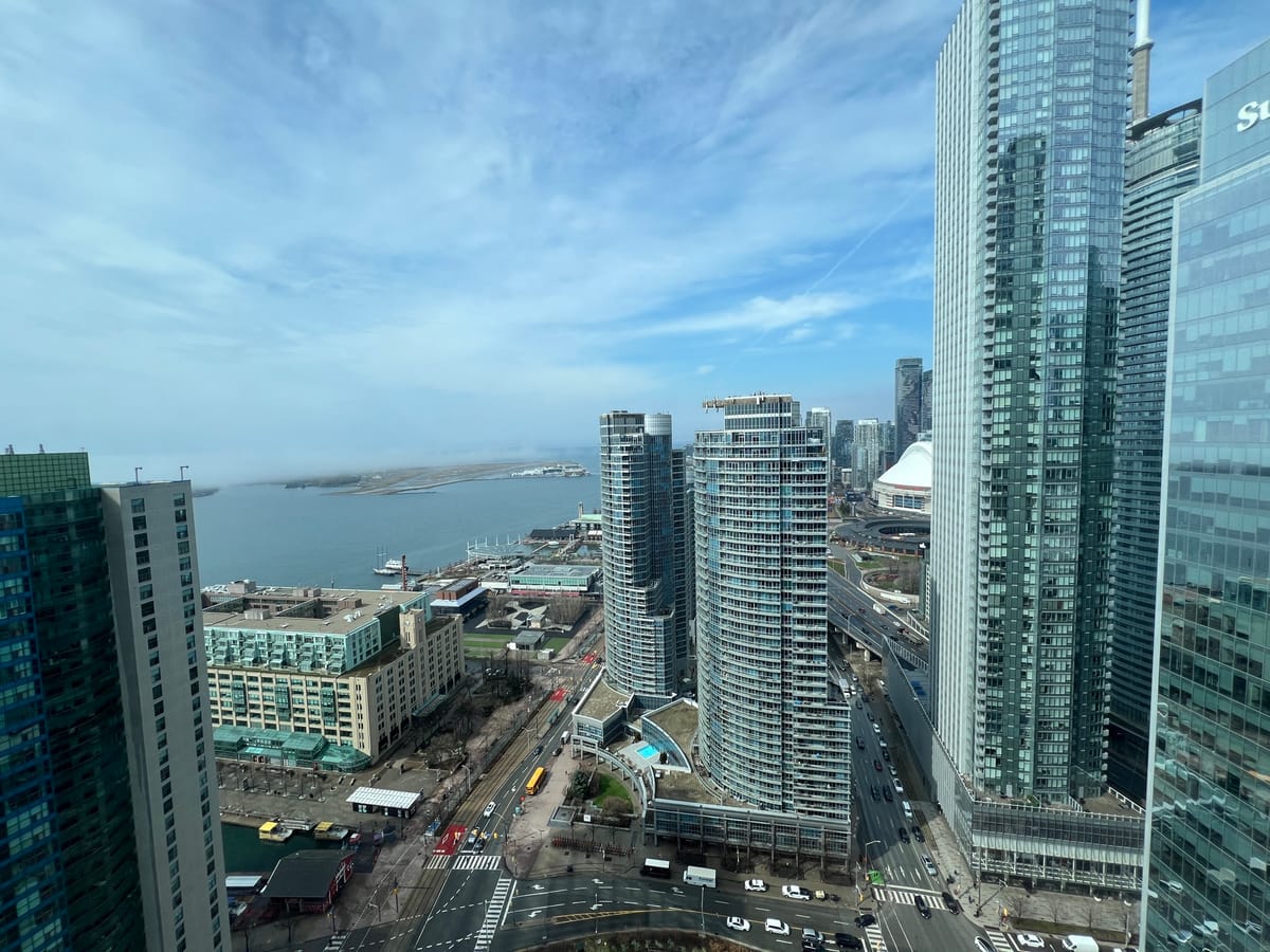 Blue sky and tall buildings from a 29th floor window. In the distance is Billy Bishop airport island on the great lake